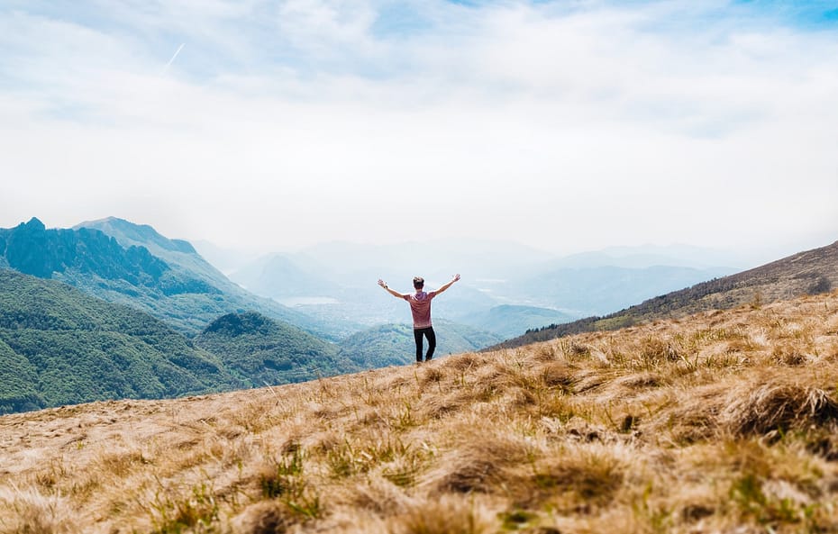 man topless standing on top of hill with dried grass field